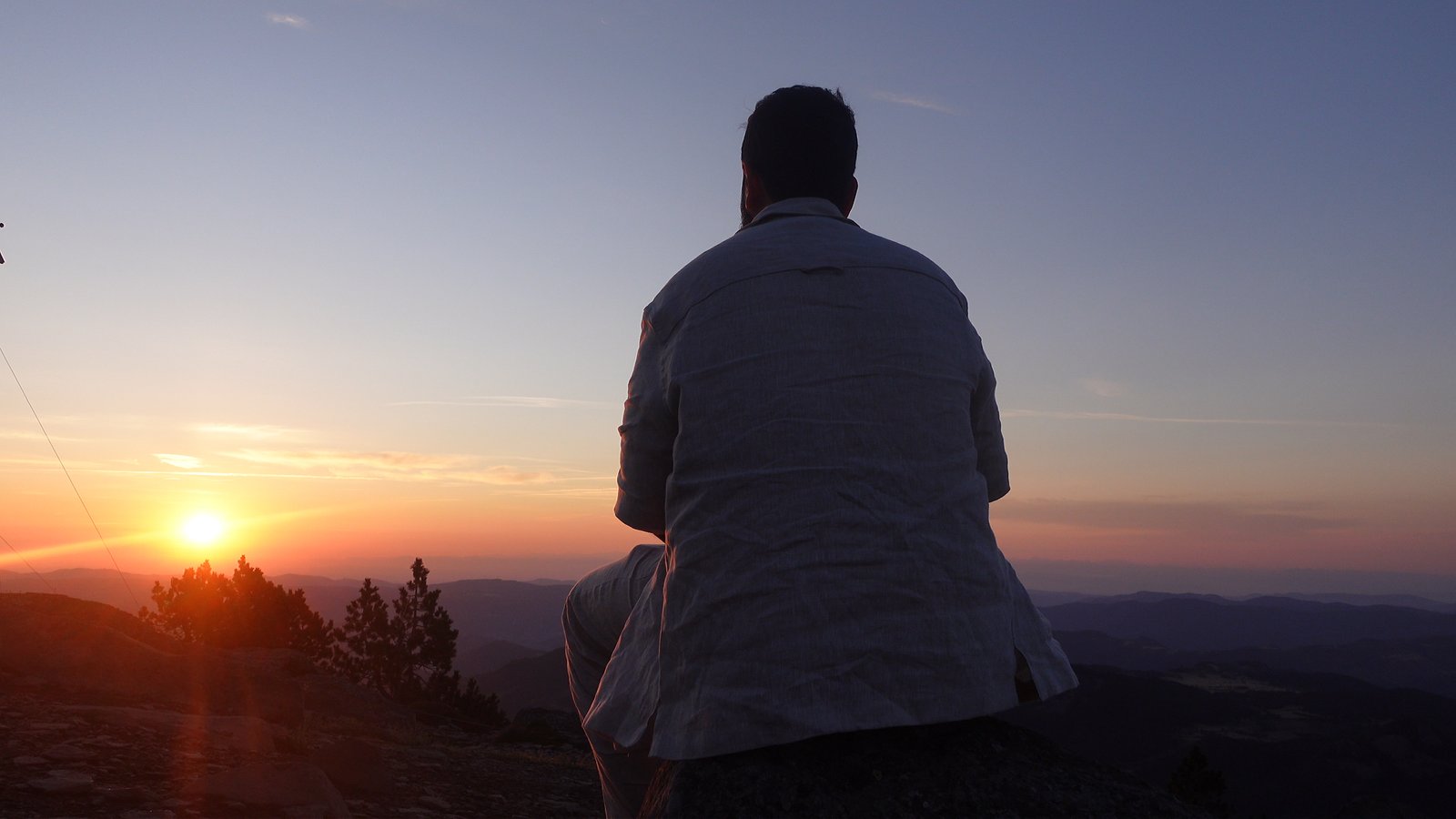 Une personne assise de dos face au soleil couchant, dans un moment de contemplation
